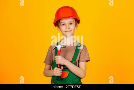 Petit constructeur dans le marteau de hardhats. Casque de construction pour enfants, casque de sécurité. Martelage par marteau. Petit constructeur en casque et hummer. Enfant habillé en ouvrier Banque D'Images