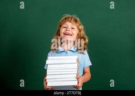 Retour à l'école. Écolier en classe. Enfant tenant la pile de livres avec le panneau de mortier sur le tableau noir Banque D'Images