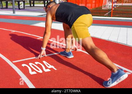 Athlète coureur dans une pose prêt à commencer sur une ligne de tapis roulant rouge avec les numéros d'inscription 2024. Le concept du début de la nouvelle année Banque D'Images