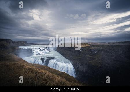 Un paysage à couper le souffle avec une chute d'eau époustouflante en cascade au milieu d'herbes vertes luxuriantes dans un environnement brumeux et nuageux Banque D'Images