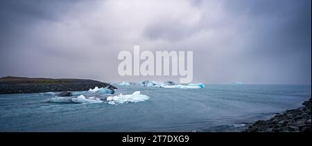 Un gros plan de deux petits morceaux de glace flottant dans une piscine d'eau avec des rochers visibles au fond Banque D'Images