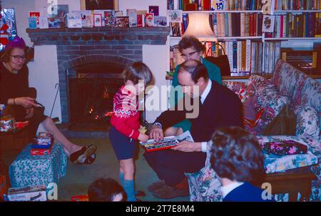 Père et fils avec cadeau de Noël le jour de Noël dans les années 1960 Grands-parents et mère regardant. De nombreux cadeaux de Noël ouverts et emballés dans la vue et des cartes de Noël. Un vrai feu en arrière-plan. Northamptonshire Angleterre 1968 Banque D'Images