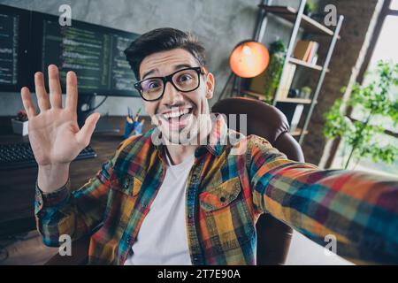 Portrait d'un homme informatique sympathique et joyeux assis chaise prendre selfie bras paume agitant le centre d'affaires de l'espace de travail haut loft à l'intérieur Banque D'Images