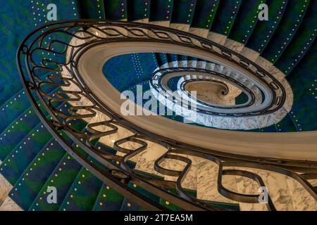 Vue d'un escalier circulaire en marbre avec un tapis bleu et vert et une rampe d'escalier en fer vue d'en haut Banque D'Images