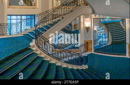 Vue d'un escalier circulaire en marbre avec un tapis bleu et vert et une rampe d'escalier en fer vue d'en haut Banque D'Images