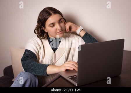 femme avec la main sur la joue assise tout en regardant l'ordinateur portable ouvert sur la table à la maison Banque D'Images
