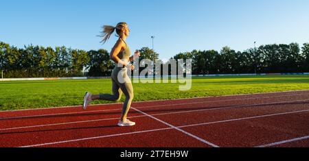 Athlète féminine courant sur un terrain d'athlétisme ensoleillé Banque D'Images