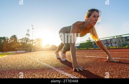 Athlète féminine en position de départ sur un terrain de piste au coucher du soleil Banque D'Images