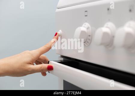 la main d'une femme appuie sur un bouton d'une cuisinière à gaz. la femme allume la lumière du four. utilisation d'une cuisinière à gaz. gros plan Banque D'Images