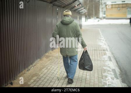 Le pensionné marche avec le sac dans sa main. Homme avec bâton de marche. Homme dans la rue. Banque D'Images