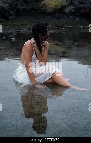 Une femme brune en costume blanc profite d'un moment de détente en profitant des thérapies à l'eau de mer Banque D'Images