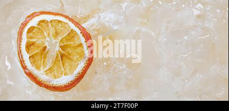 Un morceau de fruit orange sur un jus avec plein de glace sur la surface Banque D'Images