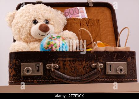 Un ours en peluche est assis dans une vieille valise avec un globe terrestre, Banque D'Images