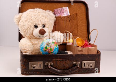 Un ours en peluche est assis dans une vieille valise avec un globe terrestre, Banque D'Images