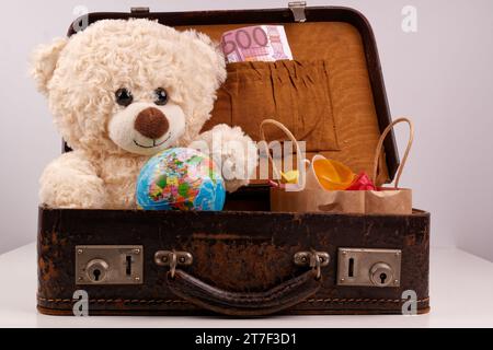 Un ours en peluche est assis dans une vieille valise avec un globe terrestre, Banque D'Images