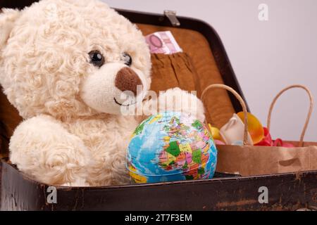 Un ours en peluche est assis dans une vieille valise avec un globe terrestre, Banque D'Images