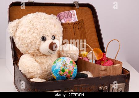 Un ours en peluche est assis dans une vieille valise avec un globe terrestre, Banque D'Images