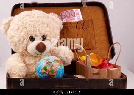 Un ours en peluche est assis dans une vieille valise avec un globe terrestre, Banque D'Images