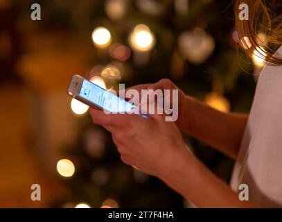 15.11.2023, Weihnachten 2023 in Deutschland, Ein festlich dekorierter Weihnachtsbaum in einer Wohnung im Unterallgäu. Eine Frau schreibt eine Weihnachts-Nachricht auf ihrem pratique. 15.11.2023, Weihnachtsbaum 15.11.2023, Weihnachtsbaum *** 15 11 2023, Noël 2023 en Allemagne, Un sapin de Noël décoré dans un appartement à Unterallgäu Une femme écrit un message de Noël sur son téléphone portable 15 11 2023, sapin de Noël 15 11 2023, sapin de Noël crédit : Imago/Alamy Live News Banque D'Images