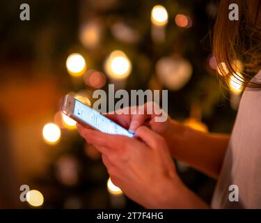 15.11.2023, Weihnachten 2023 in Deutschland, Ein festlich dekorierter Weihnachtsbaum in einer Wohnung im Unterallgäu. Eine Frau schreibt eine Weihnachts-Nachricht auf ihrem pratique. 15.11.2023, Weihnachtsbaum 15.11.2023, Weihnachtsbaum *** 15 11 2023, Noël 2023 en Allemagne, Un sapin de Noël décoré dans un appartement à Unterallgäu Une femme écrit un message de Noël sur son téléphone portable 15 11 2023, sapin de Noël 15 11 2023, sapin de Noël crédit : Imago/Alamy Live News Banque D'Images