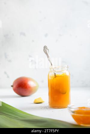Bol en verre avec cuillère de purée de confiture de mangue biologique fraîche sur fond clair avec feuille. Banque D'Images