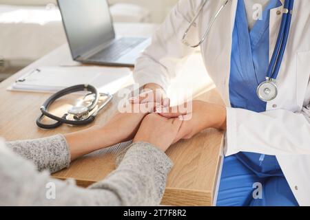 Photo en gros plan d'une jeune femme médecin tenant les mains de son patient dans les paumes. Banque D'Images