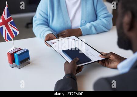 Jeune femme afro-américaine gestionnaire du centre de demande de visa passant des documents au demandeur masculin sur le bureau après approbation Banque D'Images