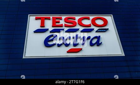 Gros plan du panneau de supermarché Tesco Extra sur un fond mural carrelé bleu. Banque D'Images