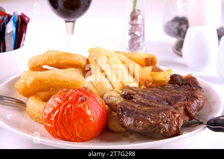 steak d'aloyau avec champignons, tomates grillées, frites et rondelles d'oignon avec verre de vin et condiments dans le baackground. Banque D'Images