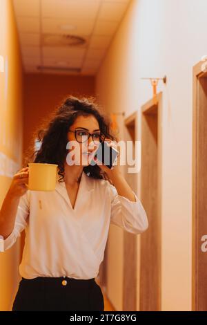 Une femme d'affaires moderne aime travailler, marcher dans une salle animée, savourer du thé et négocier un nouveau projet au téléphone. Banque D'Images