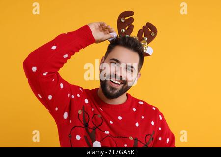 Heureux jeune homme en pull de Noël et bandeau de renne sur fond orange Banque D'Images