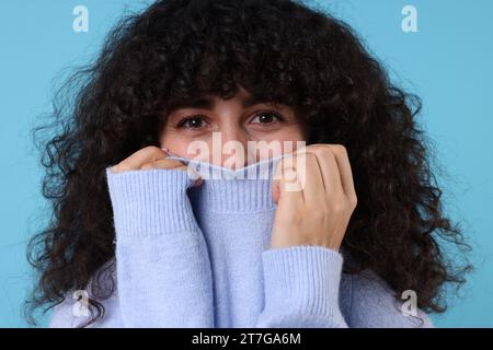 Jeune femme en pull chaud élégant sur fond bleu clair Banque D'Images