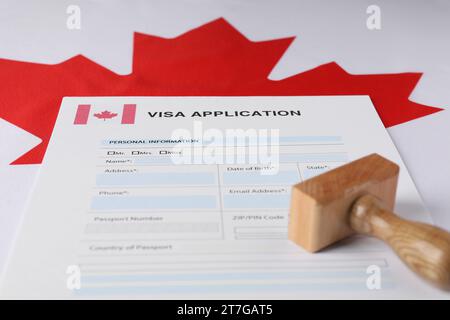 Immigration au Canada. Formulaire de demande de visa et timbre en bois sur le drapeau, closeup Banque D'Images