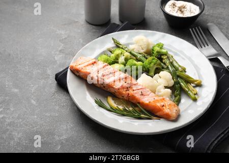 Repas sain. Morceau de saumon grillé, légumes, asperges et romarin servi sur une table texturée grise, gros plan. Espace pour le texte Banque D'Images