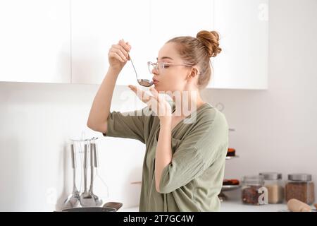 Jolie jeune femme goûtant la nourriture de louche dans la cuisine légère Banque D'Images