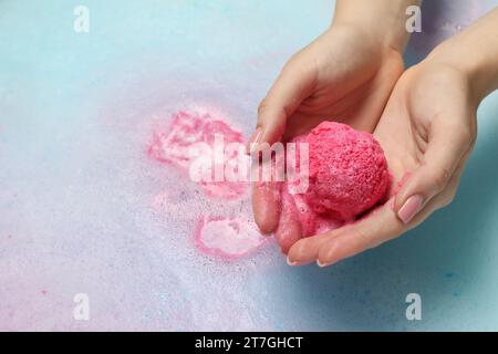 Femme tenant la bombe de bain au-dessus de l'eau avec de la mousse, gros plan. Espace pour le texte Banque D'Images