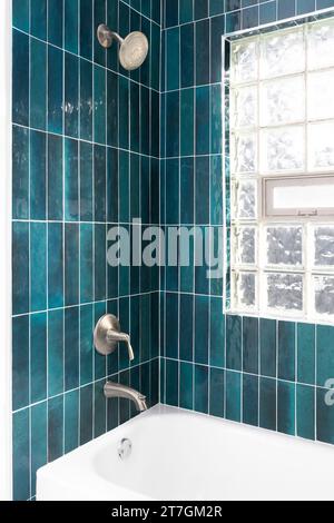 Un détail de douche de salle de bain avec des carreaux de métro verticaux en verre bleu vibrant et une fenêtre avec des blocs de verre. Banque D'Images