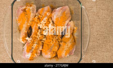 Pilons de poulet marinés avec de l'ail, de la sauce soja et du curcuma en gros plan dans un plat en verre prêt à être cuit Banque D'Images