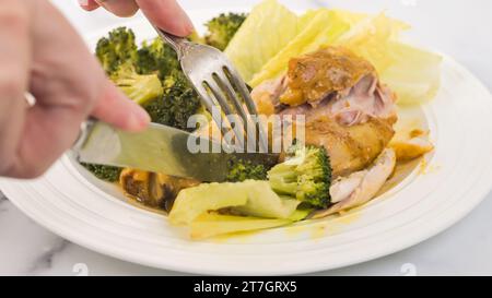 Pilons de poulet cuits avec du brocoli et servis avec de la laitue verte. Délicieux repas sur une assiette blanche gros plan sur une table de cuisine Banque D'Images