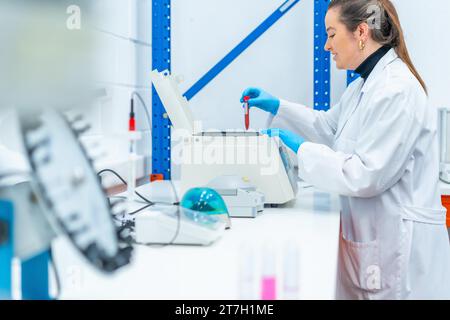 Vue latérale d'un scientifique souriant plaçant un échantillon de sang dans une centrifugeuse dans un laboratoire de recherche Banque D'Images