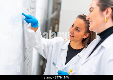 Scientifique lisant les données d'un tableau blanc dans un laboratoire à côté d'un collègue Banque D'Images