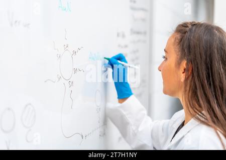 Photo en gros plan d'un scientifique menant une étude et utilisant un tableau blanc pour écrire des données avec une bourse dans un laboratoire Banque D'Images