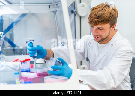 Vue latérale d'un jeune et heureux scientifique pipetant des échantillons médicaux dans des microplaques en laboratoire Banque D'Images