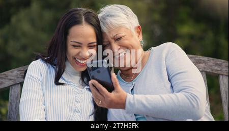 Senior, mère et femme avec smartphone sur le banc, nature et rire pour le meme des médias sociaux à la retraite. Parent mature, fille aînée et Banque D'Images