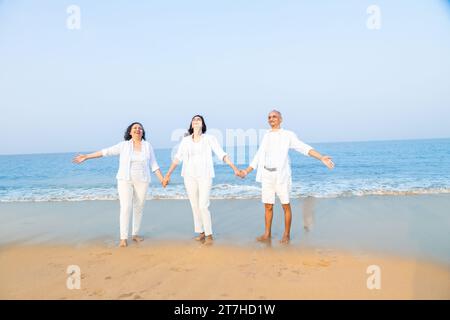 Heureux couple indien senior avec belle jeune fille profitant de vacances à la plage. Famille portant des chiffons blancs s'amusant ensemble. Banque D'Images