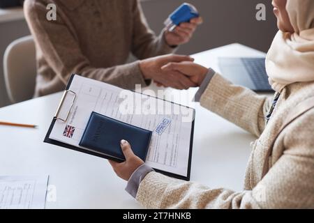 Gros plan du formulaire de demande de visa approuvé et du passeport en main de la jeune demanderesse contre sa poignée de main avec le gestionnaire tenant le timbre Banque D'Images