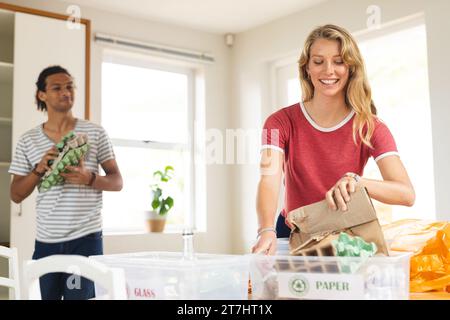 Heureux couple diversifié triant les déchets pour le recyclage dans la cuisine ensoleillée à la maison Banque D'Images