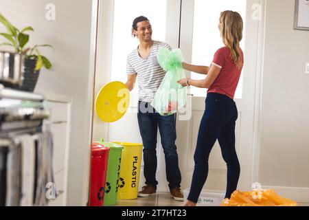 Heureux couple diversifié triant les déchets pour le recyclage dans la cuisine ensoleillée à la maison Banque D'Images