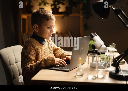 Enfant utilisant un ordinateur portable et un microscope le soir à la maison. Enseignement des sciences Banque D'Images