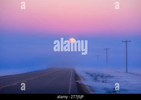 Le soleil couchant descendant dans un banc de brouillard sur une route rurale regardant plein ouest, le soir de l'équinoxe de printemps, le 20 mars 2023. Donc le Soleil est se Banque D'Images